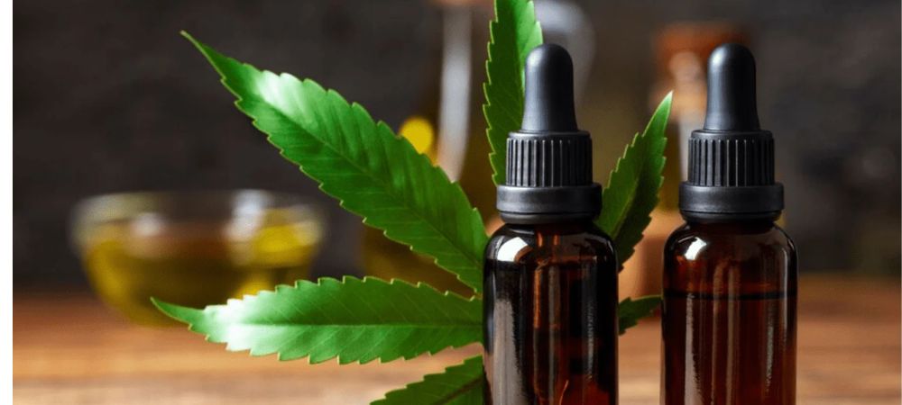 Bernsteinfarbene Glasflaschen mit Pipette und Cannabisblättern auf Holzuntergrund, Darstellung von natürlicher Kosmetik mit Cannabinoiden zur Hautpflege.